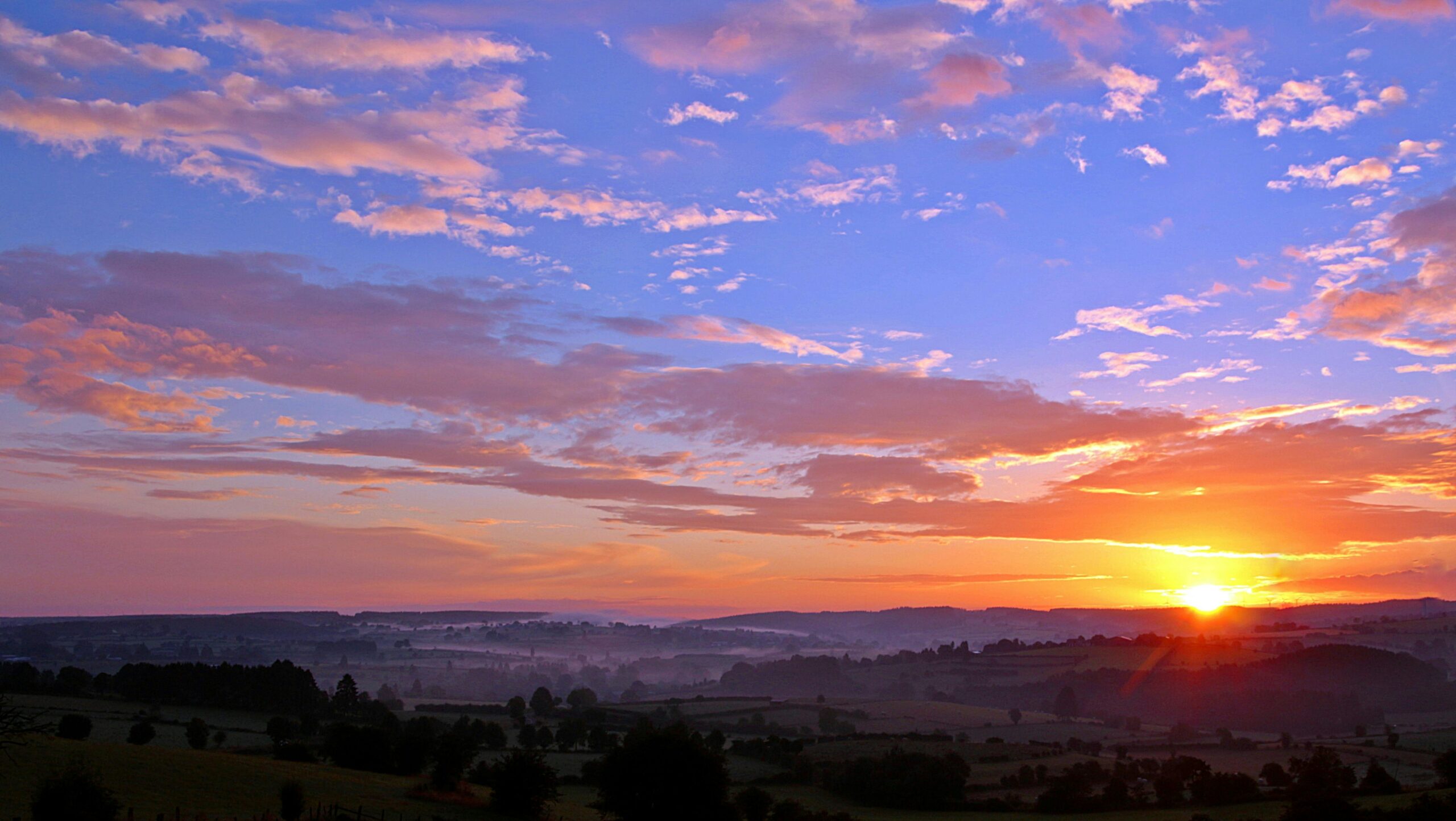 Stunning sunrise over rolling hills with colorful clouds and a vivid skyscape.